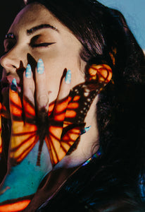 girl with butterfly on face and wearing almond shaped fake nails with clouds