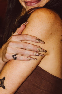 girl wearing brown top and wearing coffin shaped press on nails with wavy designs and Swarovski crystals