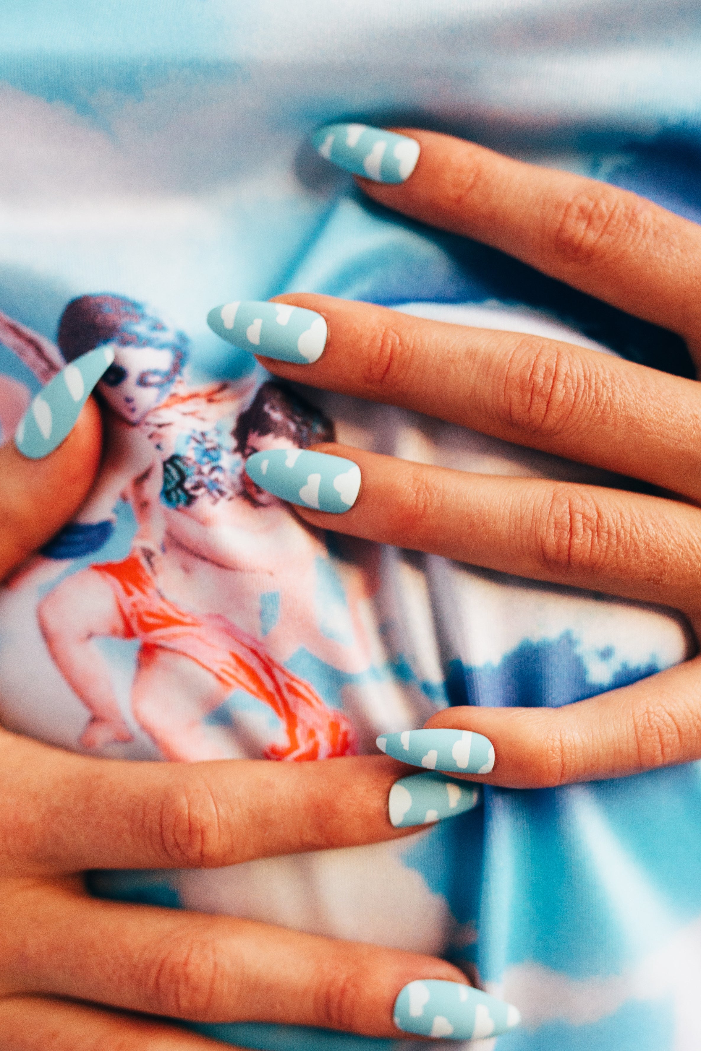two hands wearing stiletto shaped press on nails with light blue and white clouds