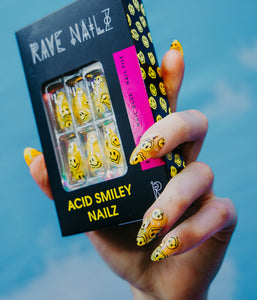wearing the Acid Smiley press on nails and holding a box of yellow dripping smiley face nails