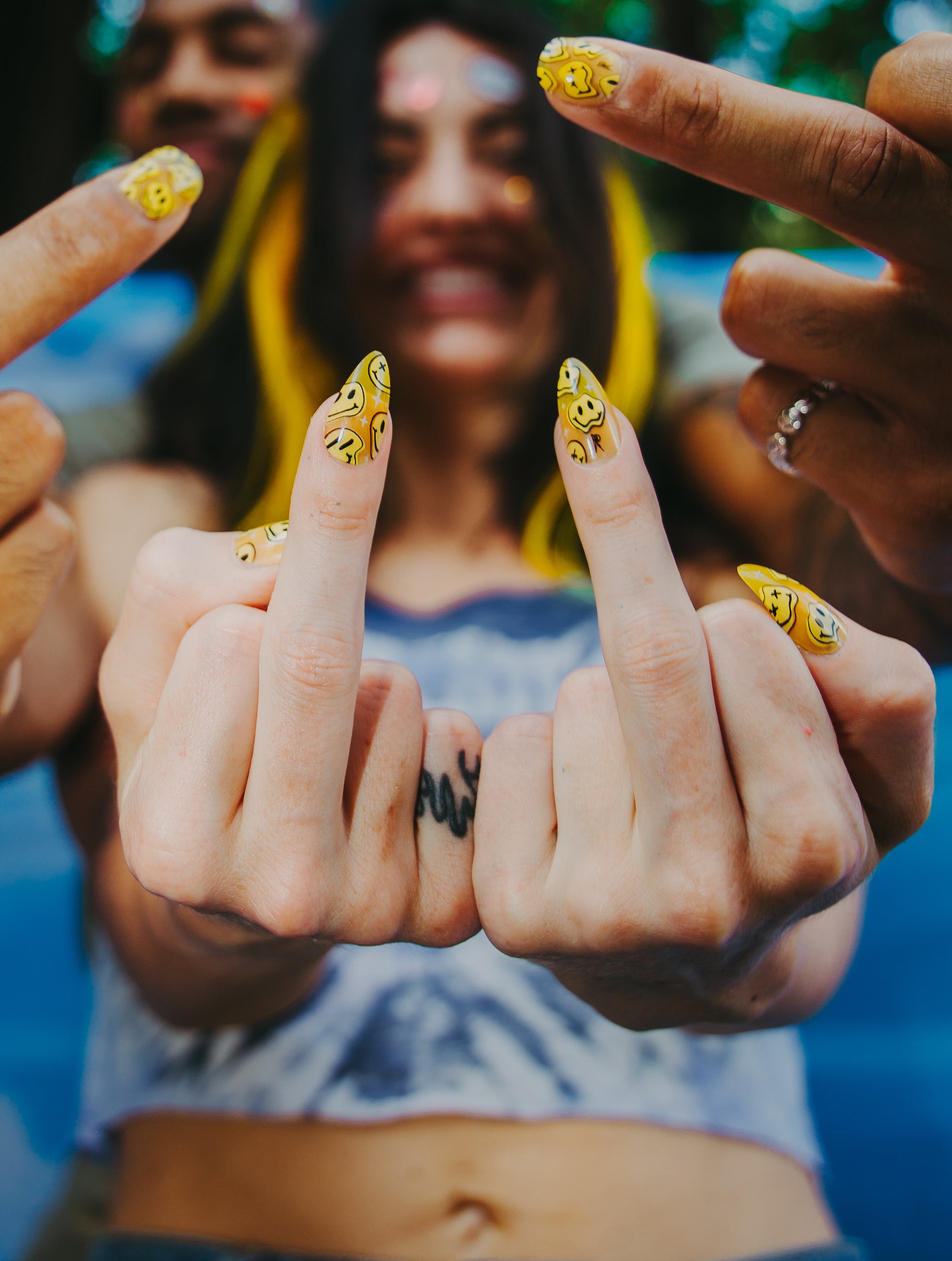 two people in 90s clothes giving the middle finger wearing yellow trippy smiley press on nails