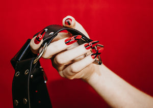 hand wearing fake nails holding a black leather harness