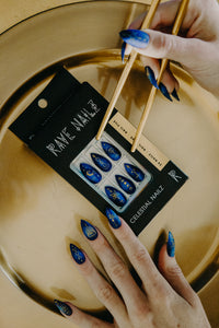 hands wearing celestial press on nails holding chopsticks with gold background and box of celestial fake nails