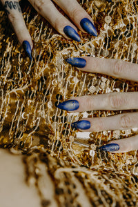 hands on a gold sequin sparkly dress wearing deep blue press on nails with gold witchy runes